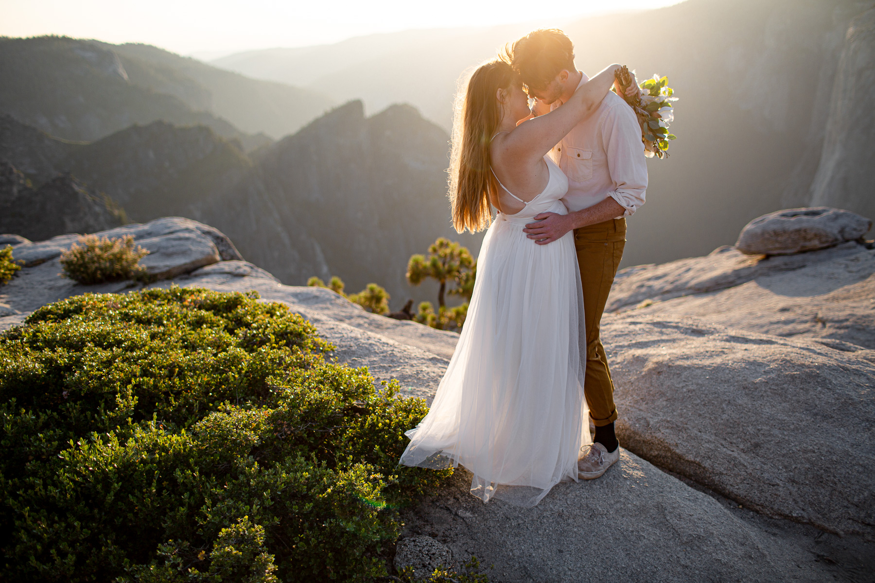 Couple cuddling on rocks on top of mountain overlooking Yosemite Valley
