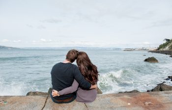 man and woman embracing while looking at the ocean