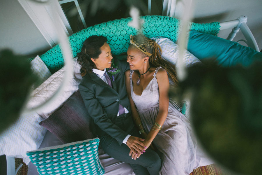 Stylish couple in wedding clothes holds hands and reclines on a green daybed