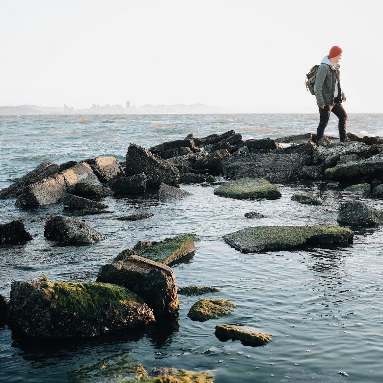 person walking on rocks near the ocean