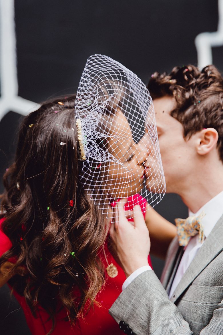 Stylish couple kissing with bride wearing a DIY birdcage veil