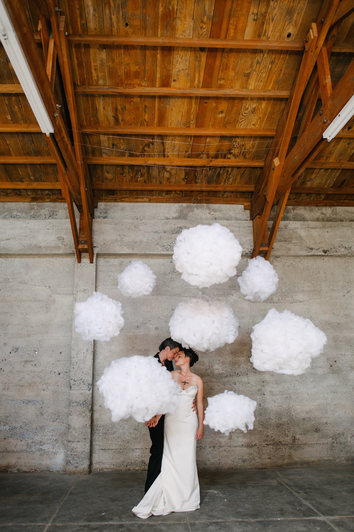 a couple stand among paper clouds hanging from the ceiling meant to be a diy photo booth backdrop