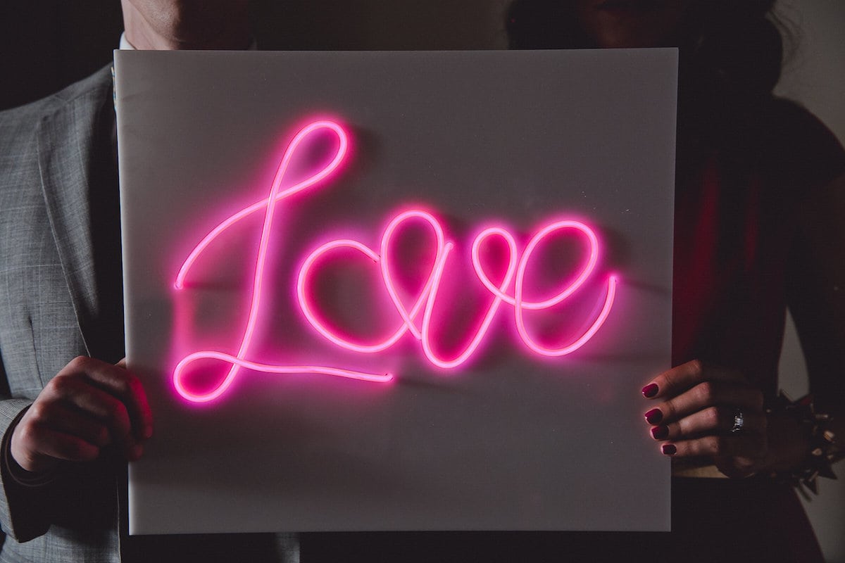 two people holding a neon sign that says love
