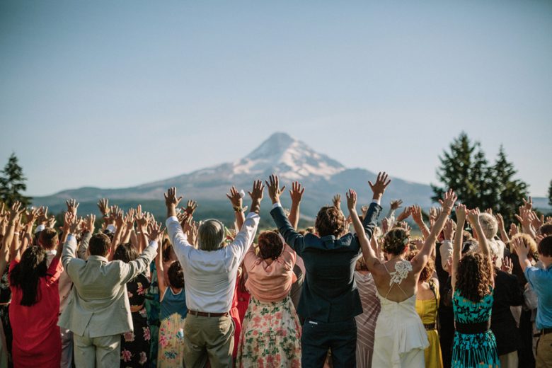 full wedding party arms in the air outside plugging in to mountain in the distance