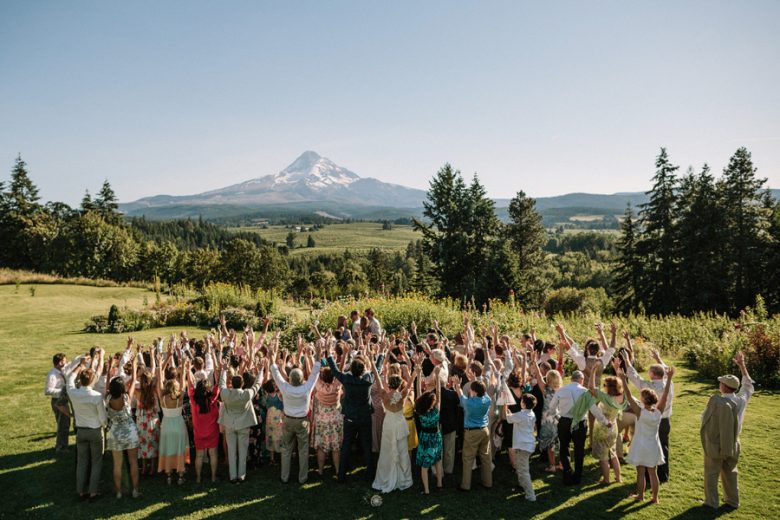 full wedding party arms in the air outside plugging in to mountain in the distance