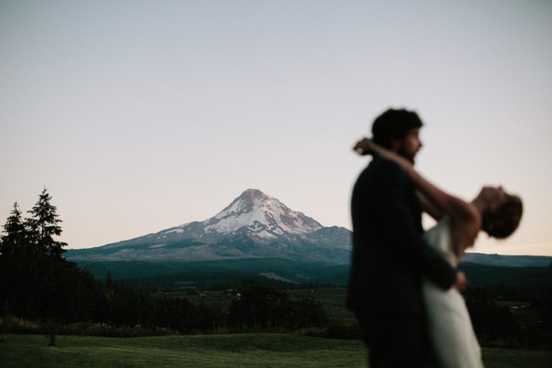 groom holding bride while she arches her back with a mountain top visible in the distance