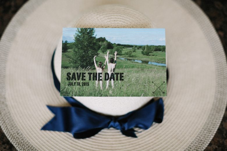 naked couple hands up in grass on wedding invite that's on a hat