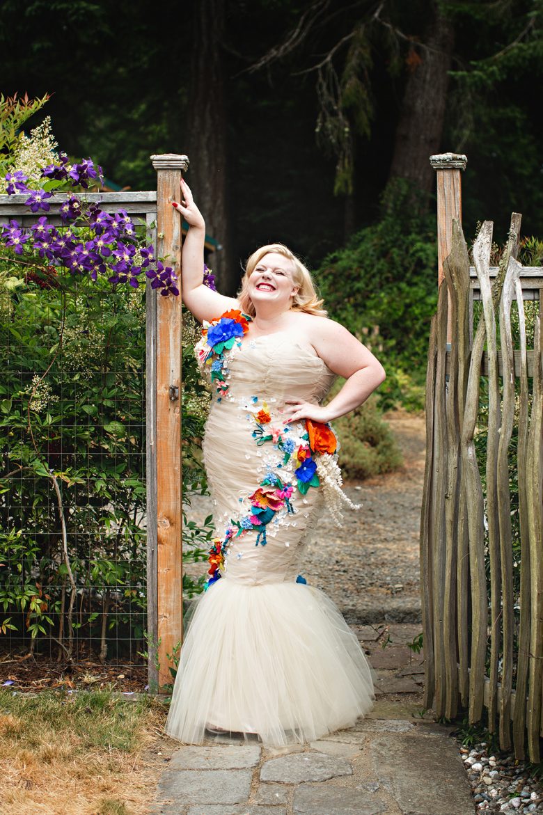 Lindy West smiling in her strapless mermaid gown by a garden fence | A Practical Wedding