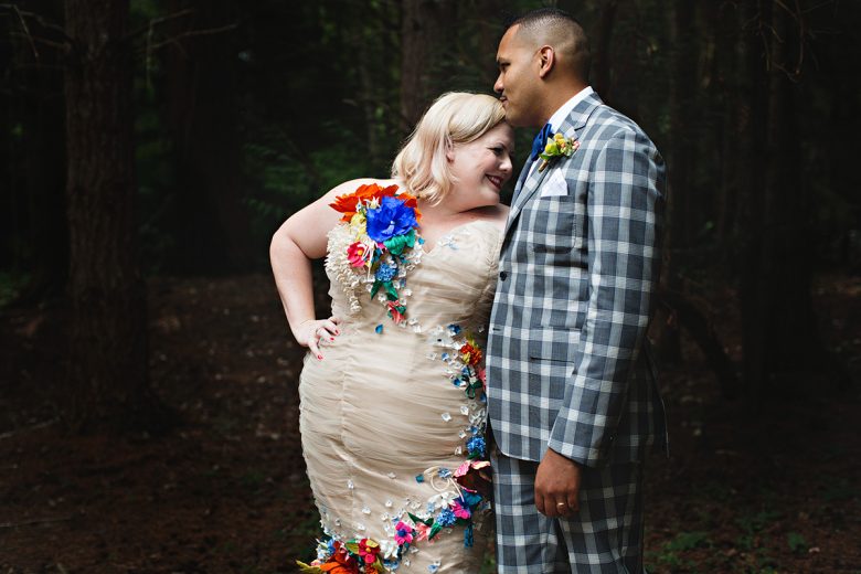 Curly haired man with plaid suit kissing the forehead of a Blonde in dress with fabric flower details | A Practical Wedding