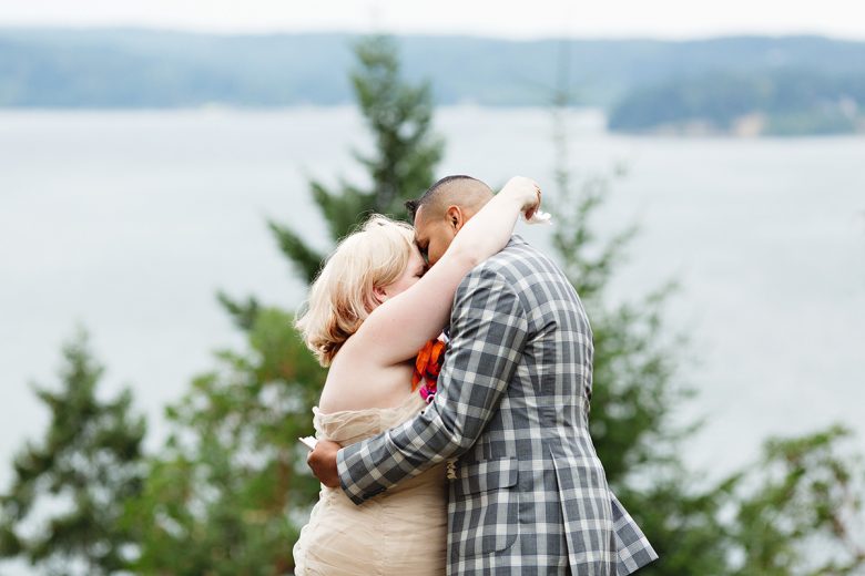 Blonde Woman and man in plaid suit kissing, with trees and water in the distance | A Practical Wedding