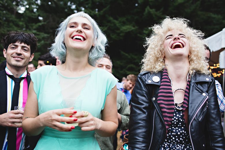 Two girls laughing with many other people laughing behind them | A Practical Wedding