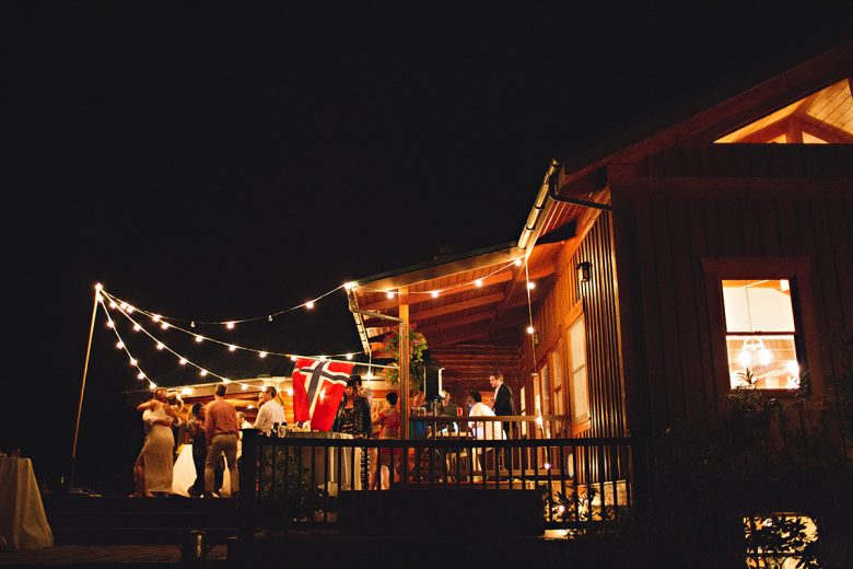 Cabin from distance at night, with people and lights and a British flag on the patio | A Practical Wedding