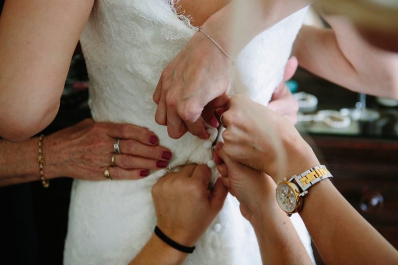 bride being helped into her wedding dress by friends and family