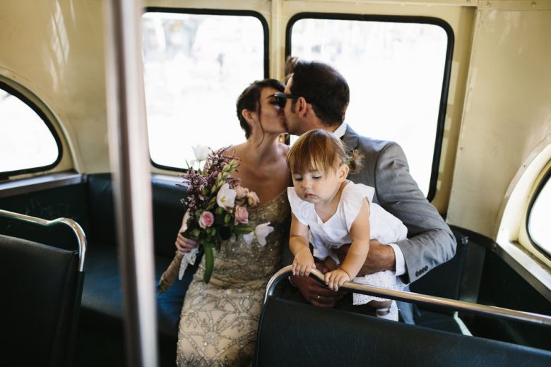 bride and groom kissing on a bus while holding their daughter