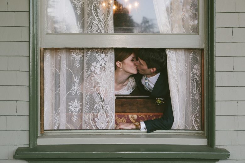 bride and groom kissing behind a window