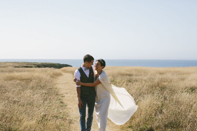 bride and groom in field in front of ocean on their wedding day