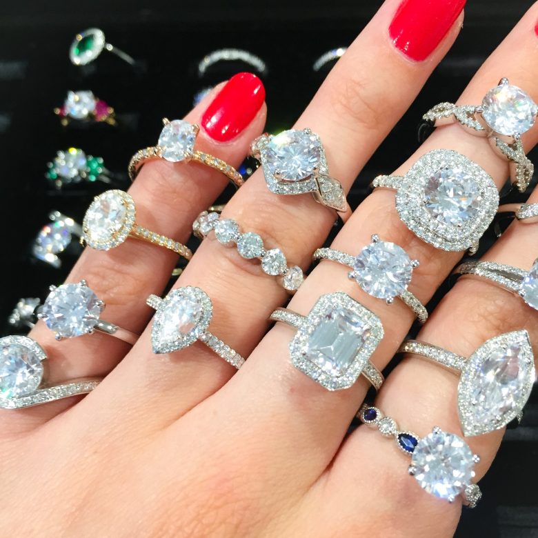 A dozen engagement rings on a hand with red fingernails