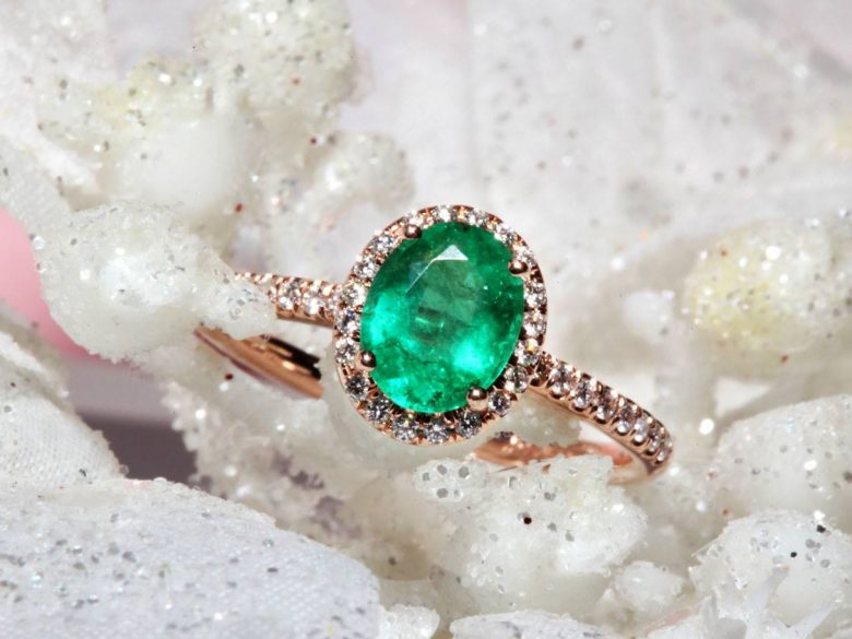 Rose gold emerald engagement ring with diamond halo on glitter backdrop