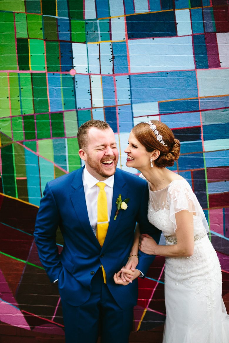Bride and groom laughing in front of colorful wall