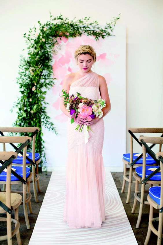 bride in a pink dress stands in front of watercolor backdrop