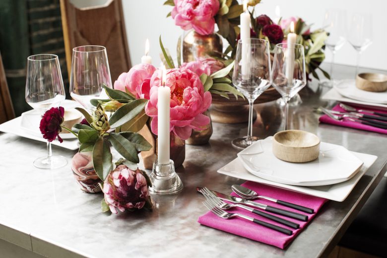 dinner table set with pink flowers, napkins, silverware, and wine glasses