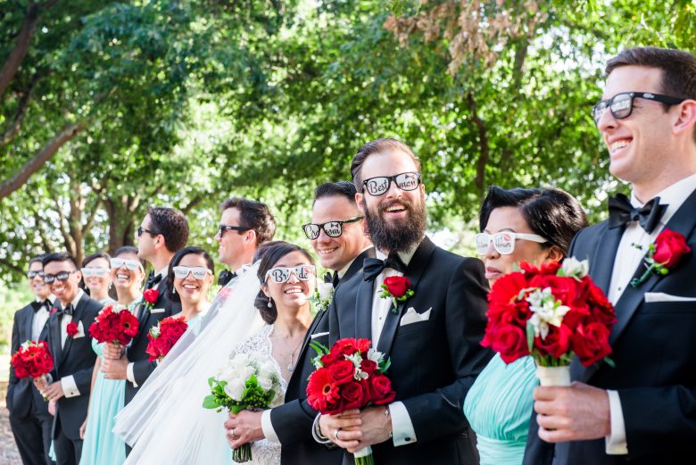 wedding party in black tuxes with red flowers and silly sunglasses