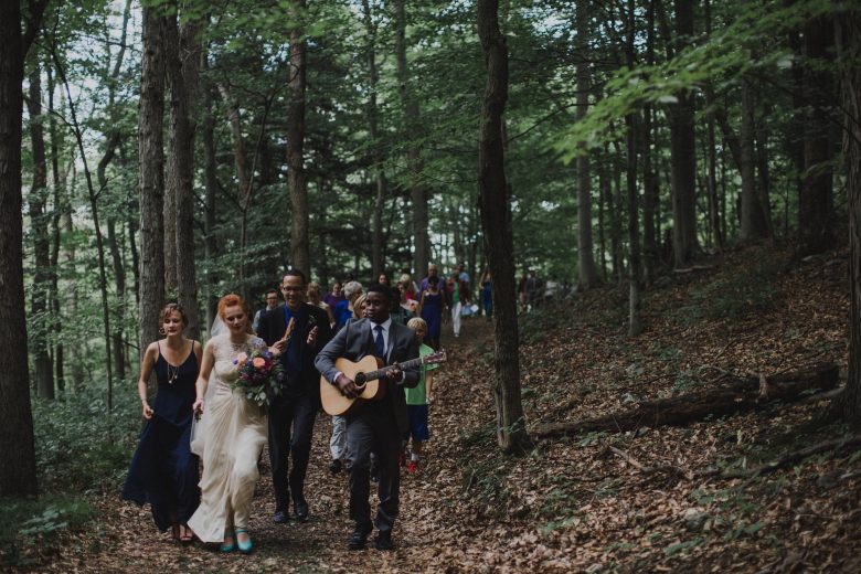 groom playing guitar and leading wedding guests to reception