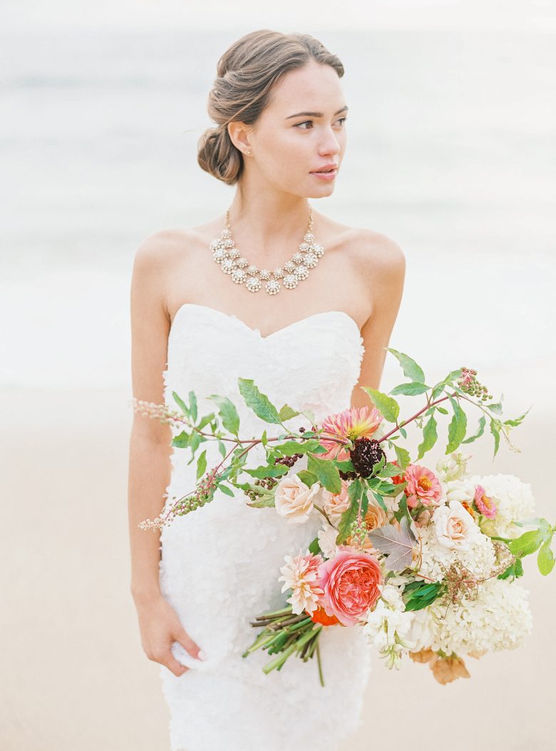 Girl with updo and statement necklace with corseted white dress holding bouquet
