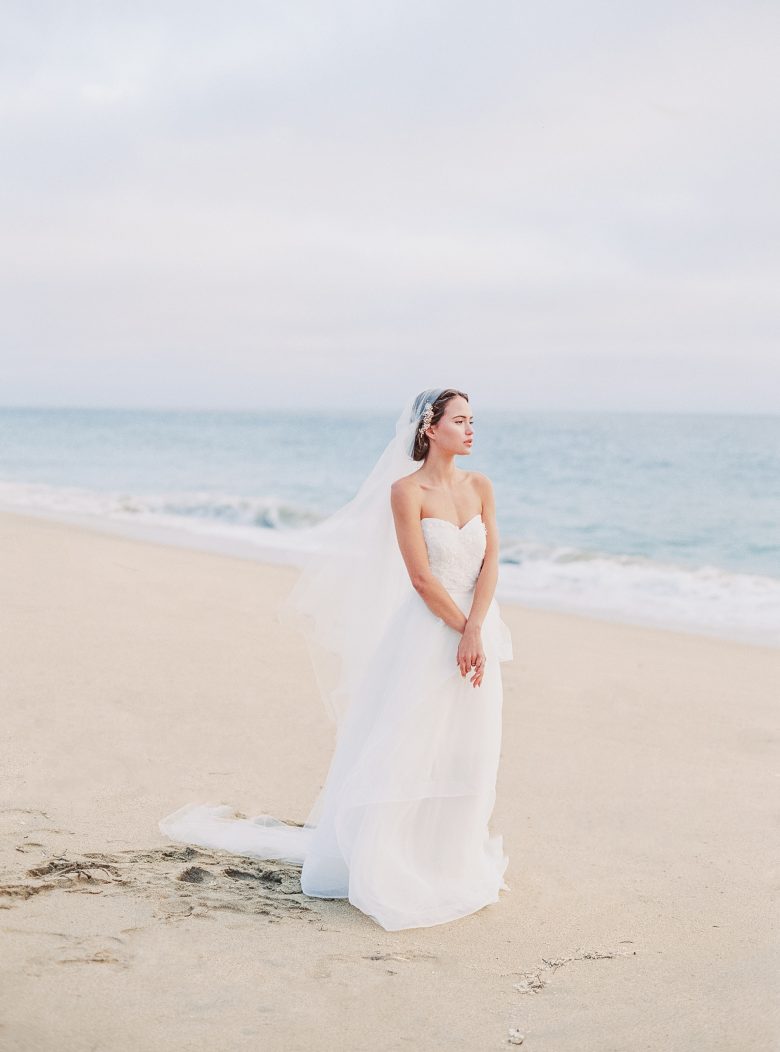 girl in white bridal outfit looking out over ocean