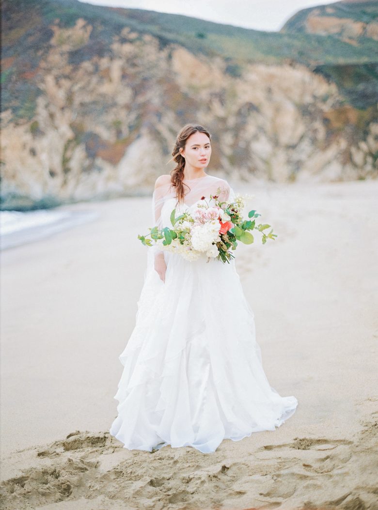 Bride in white dress on beach with muted bouquet