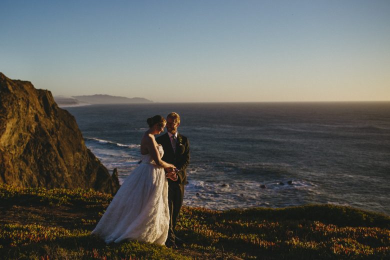Bride and groom standing together in front of the ocean