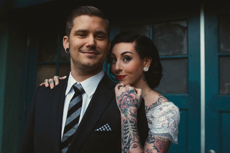 tattooed bride and groom standing in front of blue door