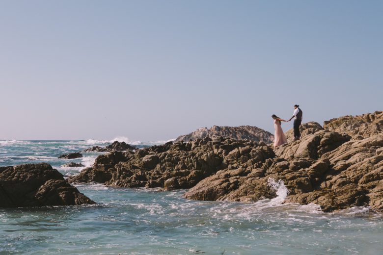 bride and groom walking on rocks next to the ocean
