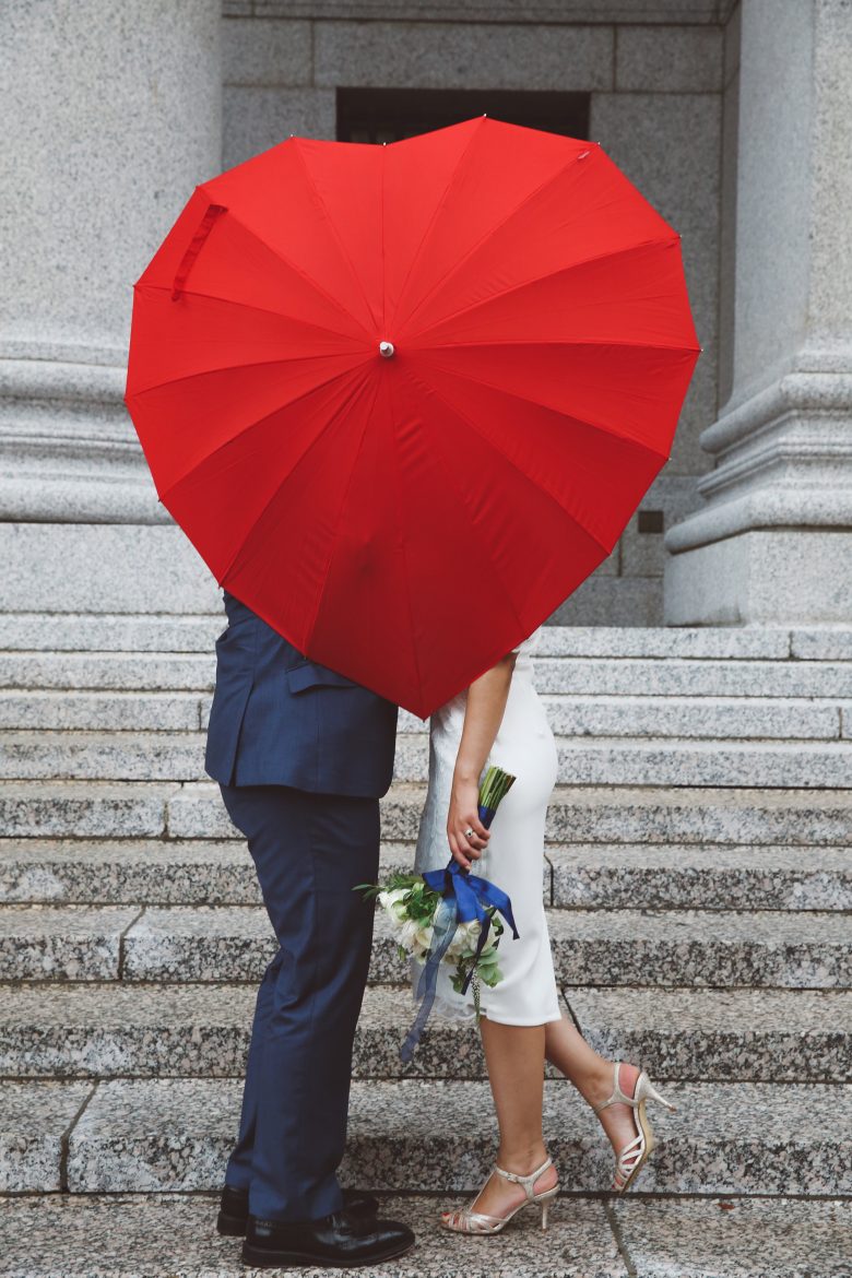 bride and groom kissing behind heart umbrella