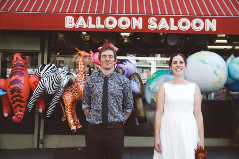 bride and groom in front of balloon saloon sign