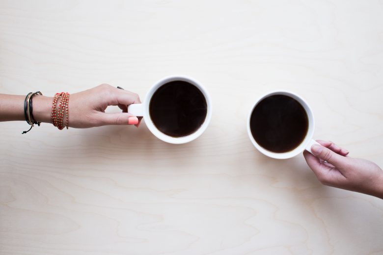 Two hands reaching towards each other with coffee mugs