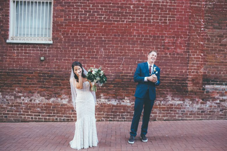 bride and groom laughing in front of a brick wall