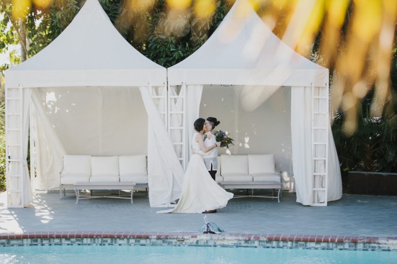 couple kissing one another next to a pool on wedding day