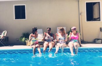 Four women sitting by the edge of a pool with drinks