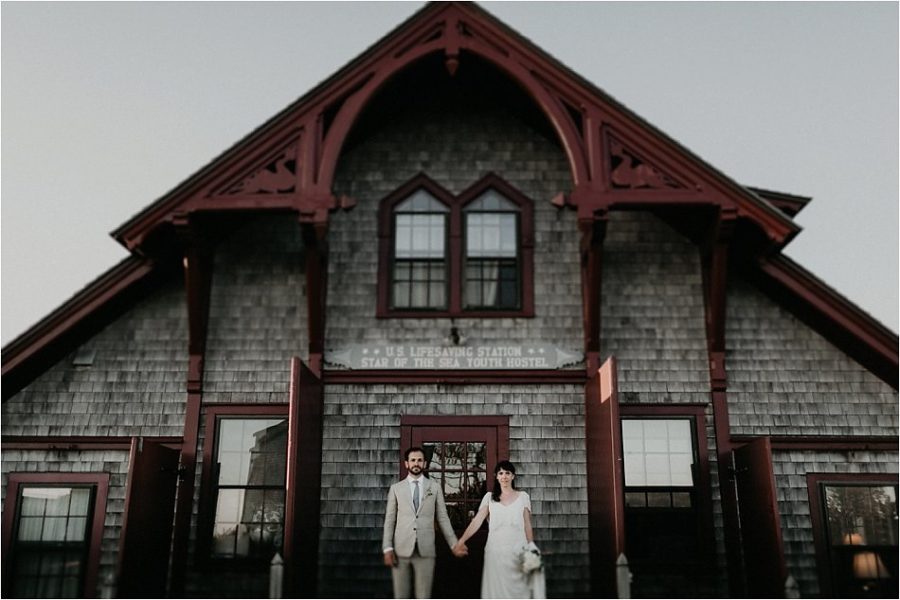 A couple in wedding clothes holding hands in front of a shingled old Nantucket building in a photo by Shaw Photography Co.