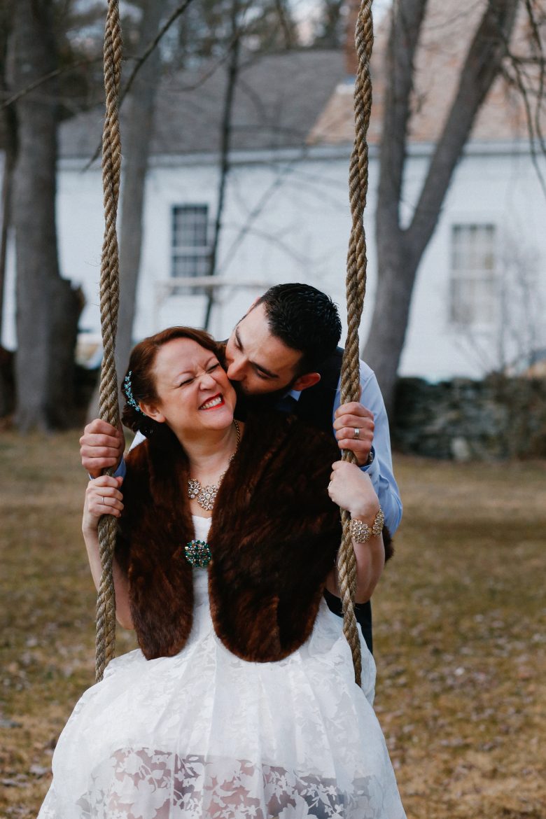 groom kissing bride who's sitting on a swing