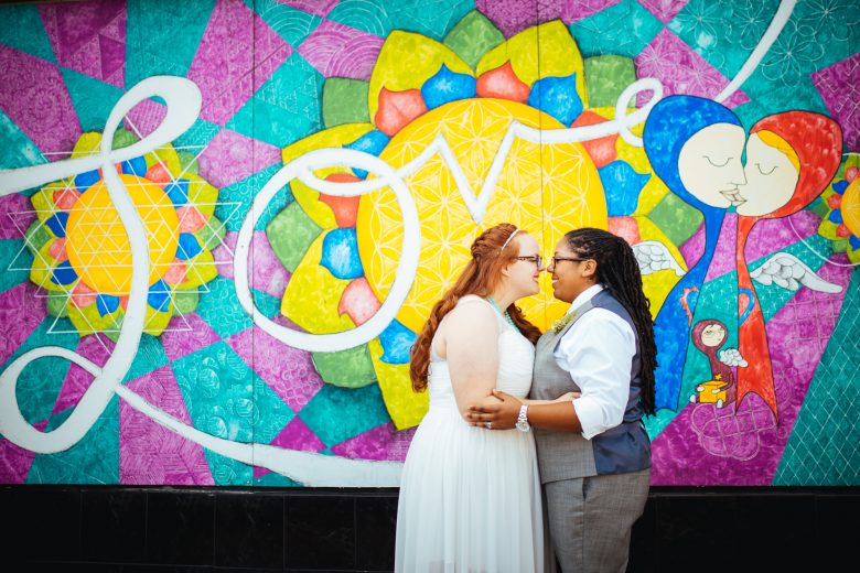 couple standing together in front of colorful love wall