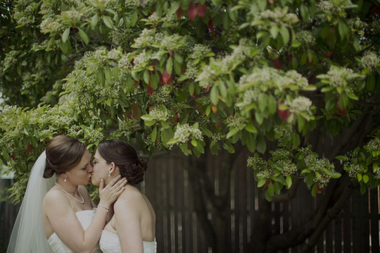 two women kissing under a tree