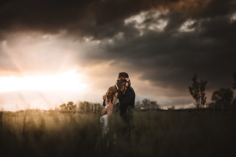 couple standing together in a field under a stormy sky