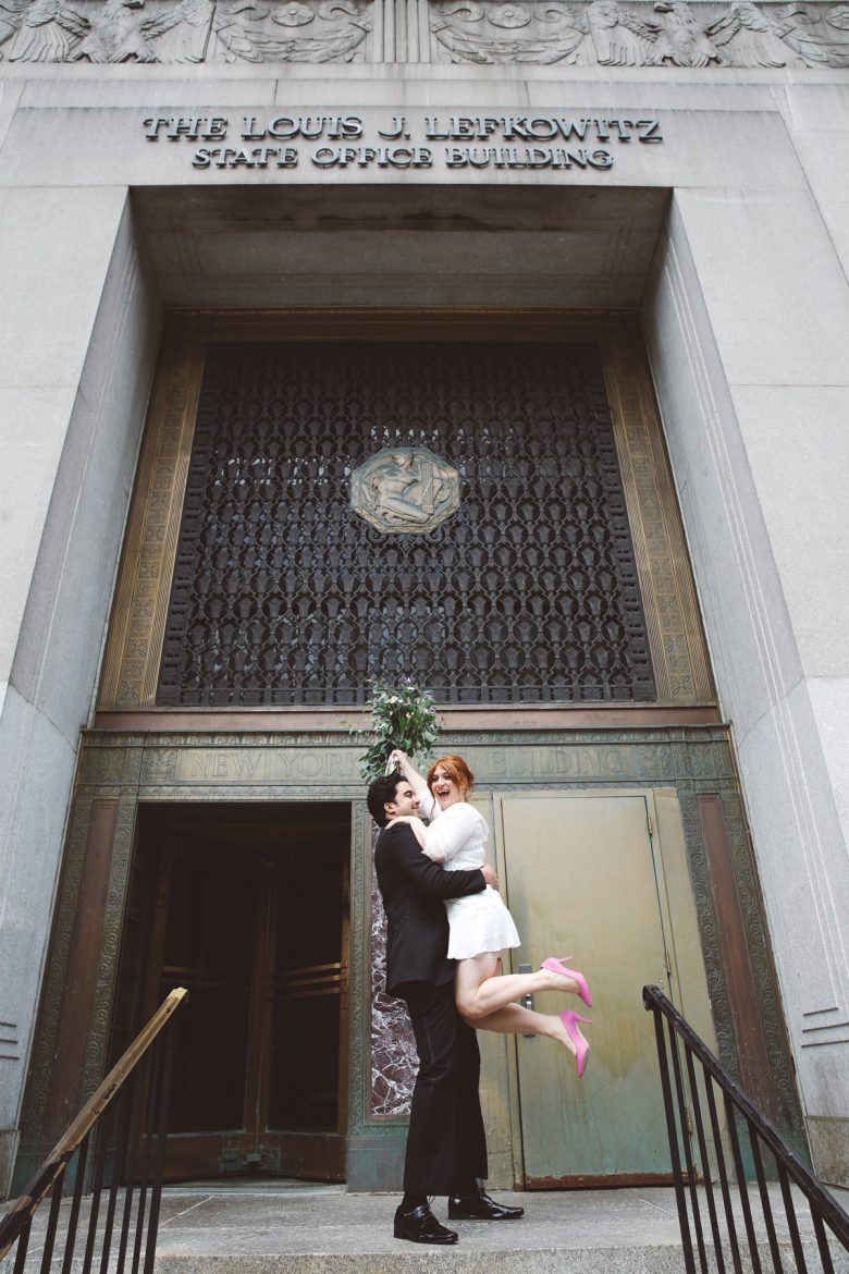 bride with pink shoes and groom embracing outside New York City Hall