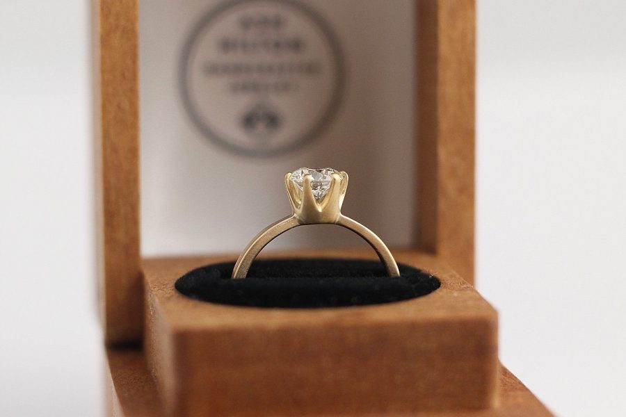 Solitaire diamond engagement ring with silver-colored band from Ash Hilton displayed in a wood ring box