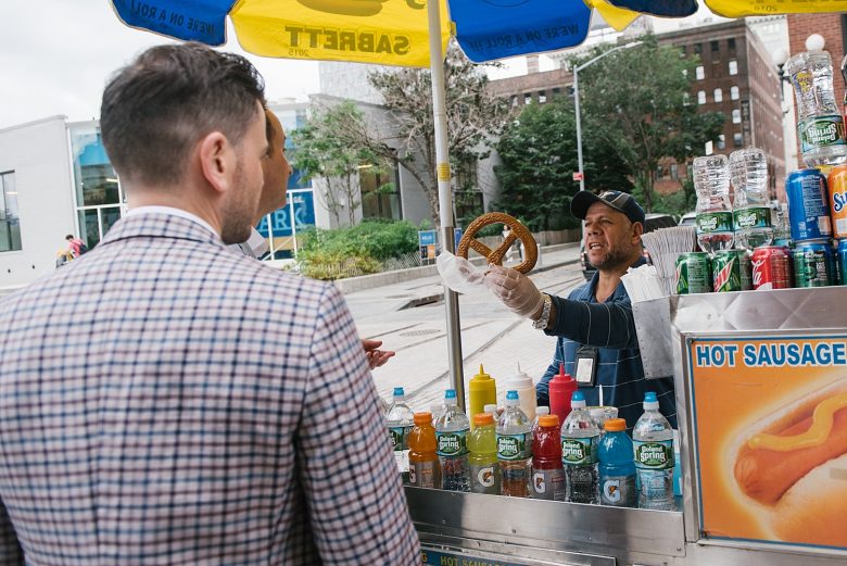 two grooms buying a pretzel from a street vendor