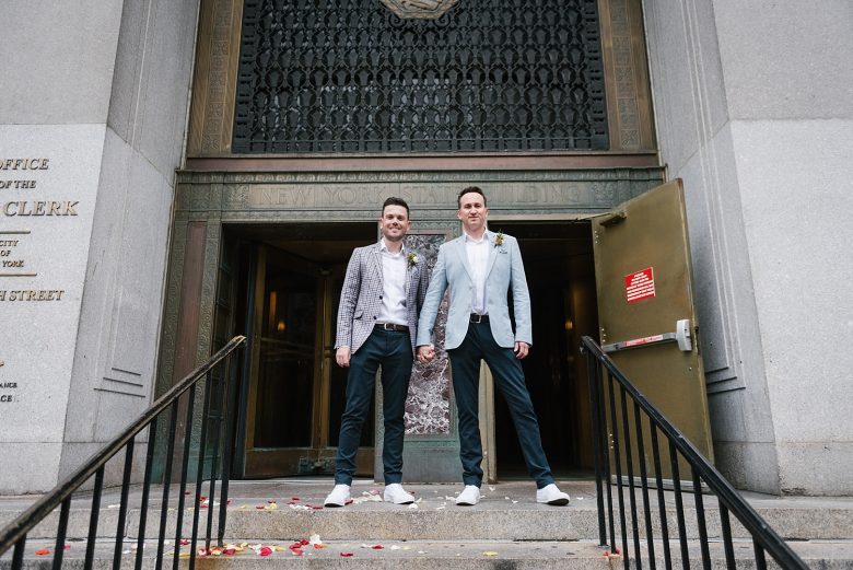 two grooms in front of the doors to New York City Hall