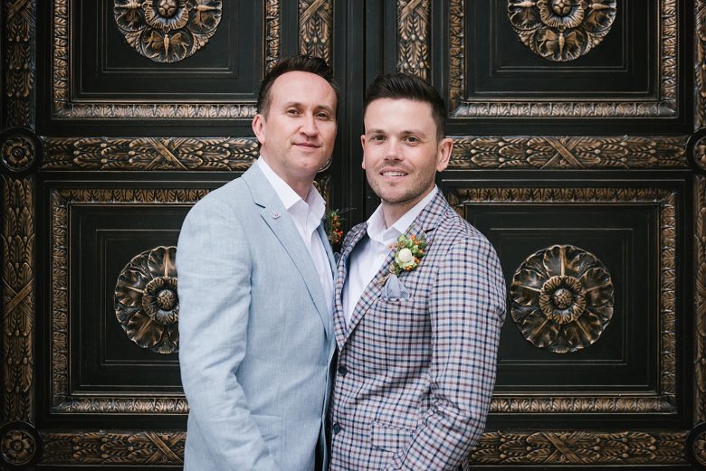 close up of two grooms in front of New York City Hall doors