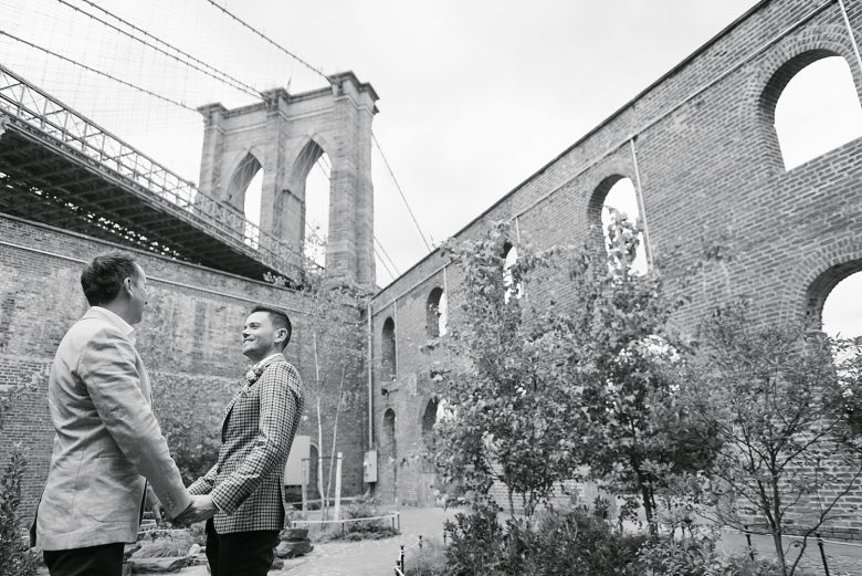 black and white portrait of two grooms at base of brooklyn bridge